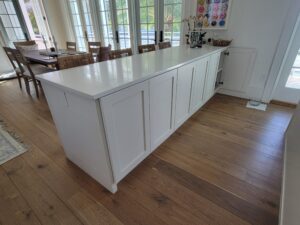 A white kitchen island with wooden floors and walls.